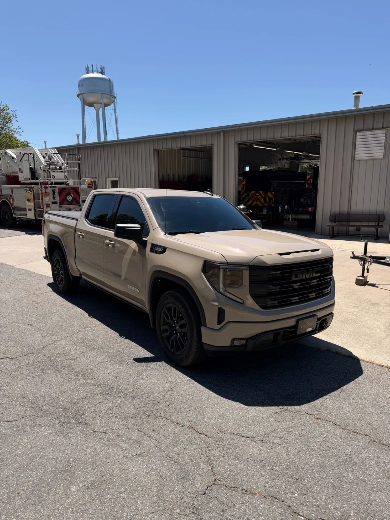 Tan GMC Sierra with dark ceramic tint parked outside a fire station